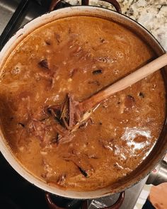 a pot filled with food sitting on top of a stove next to a wooden spoon