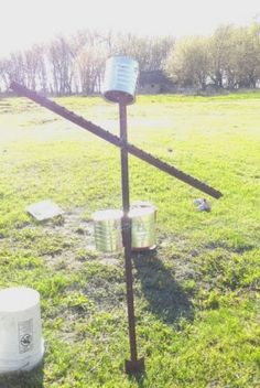 a metal pole in the middle of a field with buckets on it and an empty can next to it