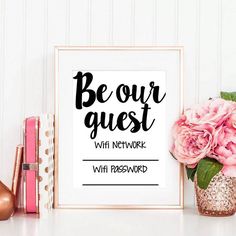 a pink flower sitting on top of a table next to a framed sign that says be our guest with network wifi password