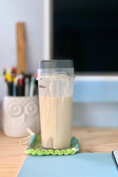 a blender sitting on top of a wooden table next to a laptop and pen