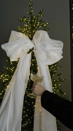 a person holding a wine glass in front of a christmas tree with lights on it