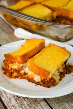 a white plate topped with two slices of lasagna casserole on top of a wooden table