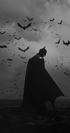 a black and white photo of a batman standing in the dark with bats flying overhead