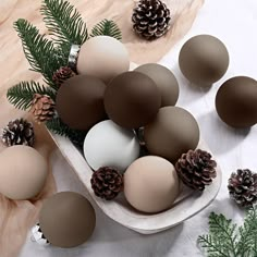 a bowl filled with lots of brown and white balls next to pine cones on top of a table