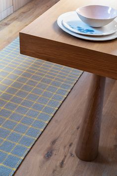 a wooden table topped with a bowl and plate next to a blue place mat on top of a wood floor