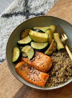 a bowl filled with salmon, rice and zucchini on top of a wooden table