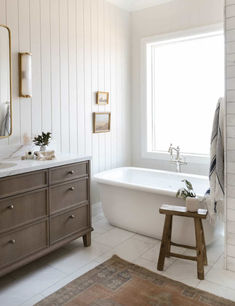 a bathroom with a white tub, wooden stool and large mirror on the wall above it