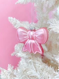 a pink bow ornament hanging from a white christmas tree with snow on it