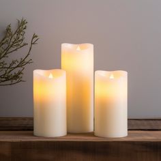 three white candles sitting on top of a wooden table