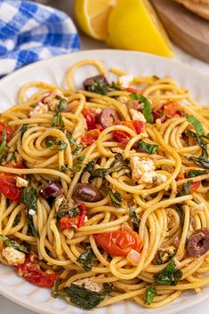 a plate of pasta with tomatoes, olives and fettuccine on it