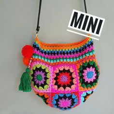 a multicolored crocheted bag hanging on a wall with a mini sign above it