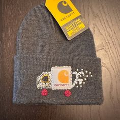 a gray beanie hat with an orange and white truck embroidered on the front, next to a yellow tag