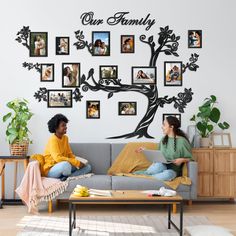 two women sitting on a couch in front of a tree with family photos hanging on it