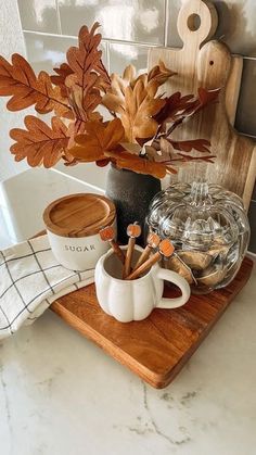 a wooden tray topped with two mugs filled with coffee and cinnamon sticks next to a potted plant