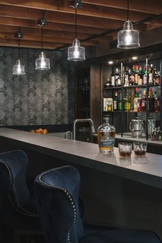 a bar with blue velvet chairs and hanging lights above it, along with liquor bottles on the shelves