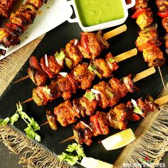 several skewers of meat and vegetables on a black plate with green dipping sauce