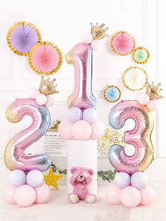 a pink teddy bear sitting on top of a white pillar next to balloons and decorations