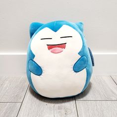 a blue and white stuffed animal sitting on top of a wooden floor next to a wall