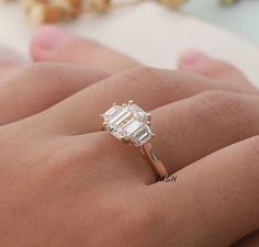 a woman's hand with a diamond ring on top of her finger and the other hand holding an engagement ring