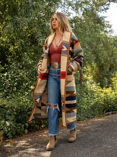 Wyeth Trail Long Stadium Coat Our Wyeth Trail Long Stadium Coat will keep you covered from top to below the knee. Made from the Pendleton Wyeth Trail wool blanket, the warm earth tone colors are easy to wear. Wear it open or close at the waist with a toggle. Designed for a slightly oversized fit and look. The Wyeth Trail blanket reflects warm, harmonious colors of ancient corn varieties patterned in rows similar to ancient Native American gardens. Arrows point in two directions, the past and the Montana Womens Fashion, Blanket Coat Outfit, Western Inspired Fall Outfits, Big Sur Style Fashion, Native Clothing Women Style, Fall 2024 Western Fashion Trends, Native American Modern Fashion, Elegant Bohemian Fashion, Cute Winter Travel Outfits