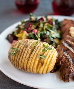 a white plate topped with steak, potatoes and salad next to glasses of red wine