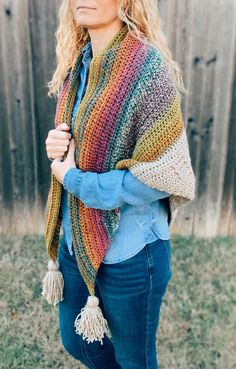 a woman standing in front of a wooden fence wearing a multicolored shawl