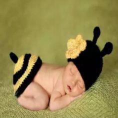 a baby wearing a black and yellow hat laying on top of a green blanket next to a stuffed animal