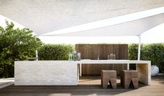 an outdoor dining area with table and stools under a white awning over it