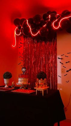 a table topped with lots of cake next to a wall covered in red string lights