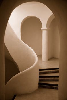 a spiral staircase in an old building with white walls and arches on either side, leading up to the second floor