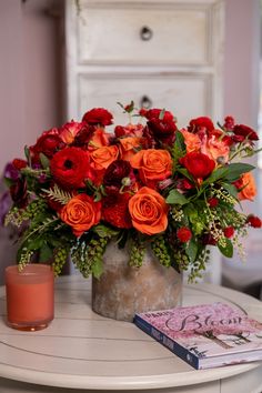 a vase filled with red and orange flowers on top of a table next to a book