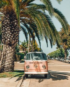 an old vw bus is parked on the side of the road next to a palm tree