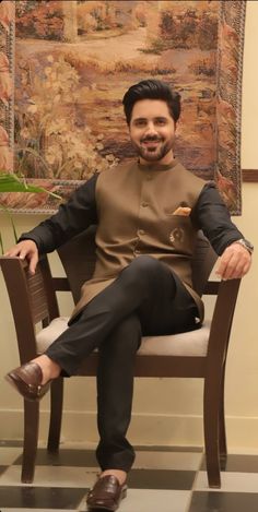 a man sitting on top of a chair in front of a wall with a painting behind him