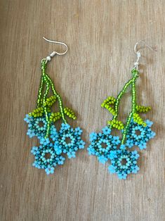 two pairs of beaded earrings with flowers on them sitting on top of a wooden table