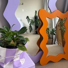 an orange and purple mirror sitting next to a potted plant