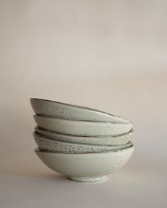 four white bowls stacked on top of each other in front of a beige background with speckles