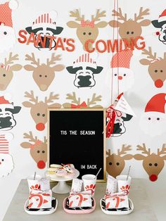 a table topped with plates and cups filled with food next to a wall covered in reindeer decorations