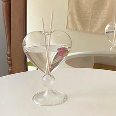 a heart shaped vase with sticks sticking out of it on a white tablecloth covered dining room table