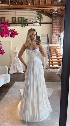 a woman in a white dress taking a selfie with her cell phone while wearing a wedding dress