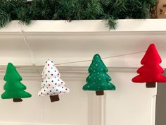 christmas trees are hanging from a string on the mantle