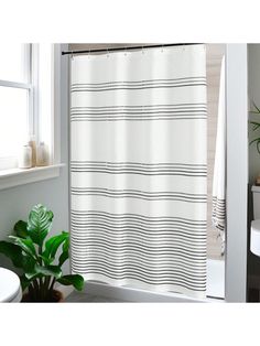 a bathroom with a white shower curtain next to a toilet and a plant in the corner