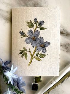 a card with blue flowers on it next to some watercolor pencils and markers