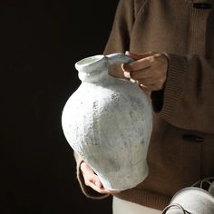 a person holding a white vase in their hands