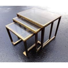 three nesting tables with glass tops and gold trimmings on the sides, sitting on a wet surface