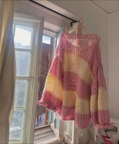 a pink and yellow sweater hanging from a window sill