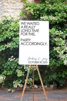 a white sign sitting on top of a wooden easel next to a lush green wall