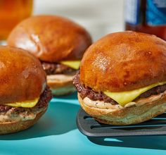 three hamburgers sitting on top of a blue tray next to a glass of beer