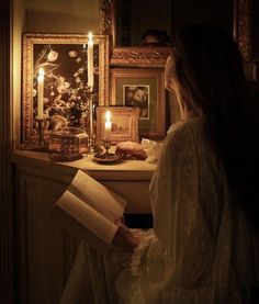 a woman sitting on a window sill reading a book with candles in front of her