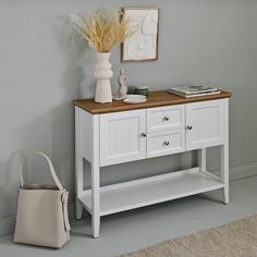 a white table with two drawers and a vase on top, next to a purse