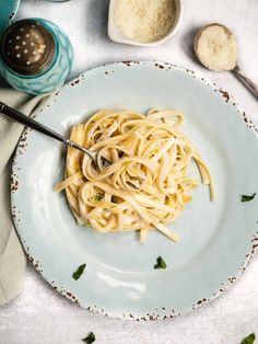 a white plate topped with pasta and parmesan cheese next to two spoons